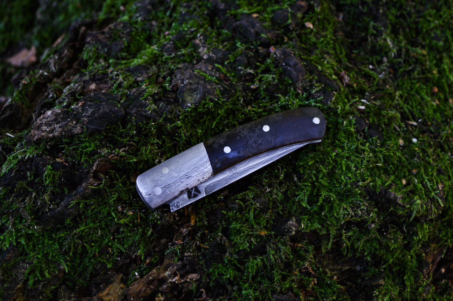 Hand-forged slipjoint folding knife with a pattern-welded blade. Wrought Iron Bolsters with Black Ash Burl Scales. Non-locking UK Legal Carry