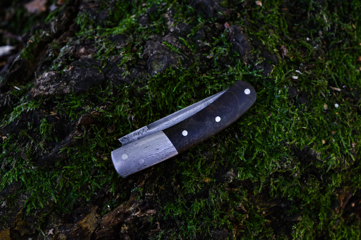 Hand-forged slipjoint folding knife with a pattern-welded blade. Wrought Iron Bolsters with Black Ash Burl Scales. Non-locking UK Legal Carry