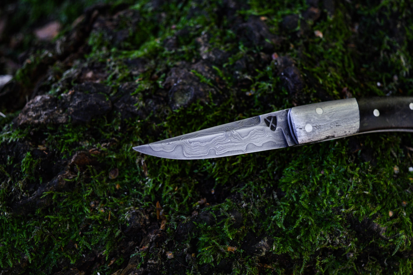 Hand-forged slipjoint folding knife with a pattern-welded blade. Wrought Iron Bolsters with Black Ash Burl Scales. Non-locking UK Legal Carry