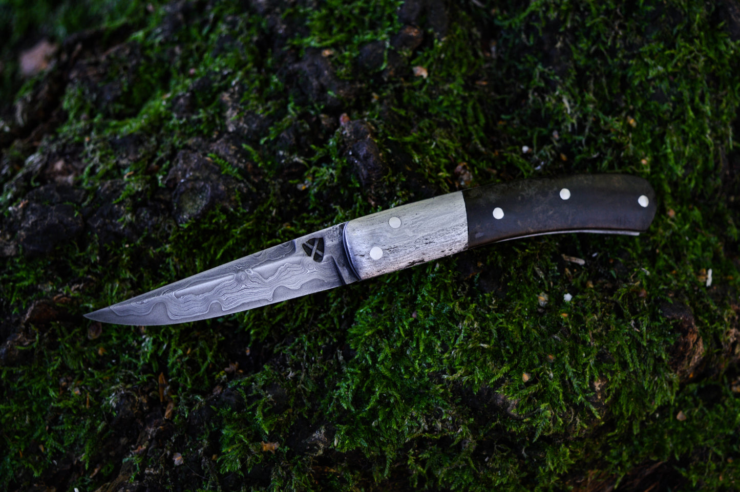 Hand-forged slipjoint folding knife with a pattern-welded blade. Wrought Iron Bolsters with Black Ash Burl Scales. Non-locking UK Legal Carry