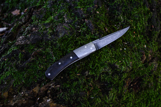 Hand-forged slipjoint folding knife with a pattern-welded blade. Wrought Iron Bolsters with Black Ash Burl Scales. Non-locking UK Legal Carry