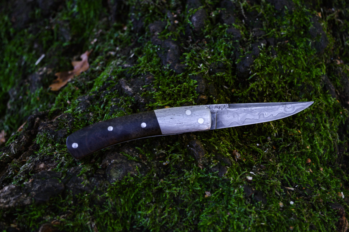 Hand-forged slipjoint folding knife with a pattern-welded blade. Wrought Iron Bolsters with Black Ash Burl Scales. Non-locking UK Legal Carry
