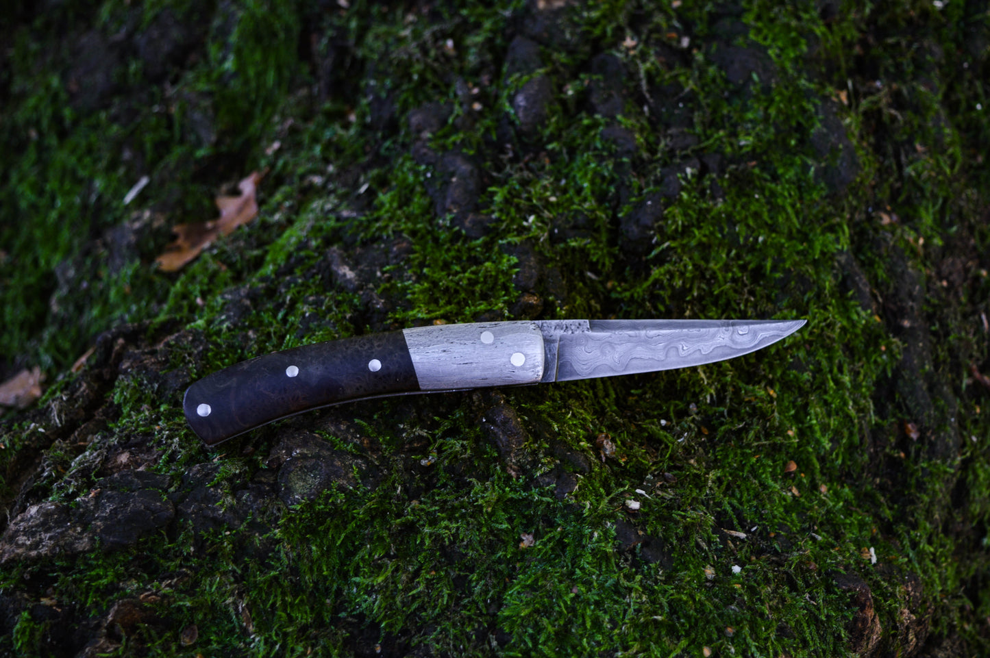 Hand-forged slipjoint folding knife with a pattern-welded blade. Wrought Iron Bolsters with Black Ash Burl Scales. Non-locking UK Legal Carry
