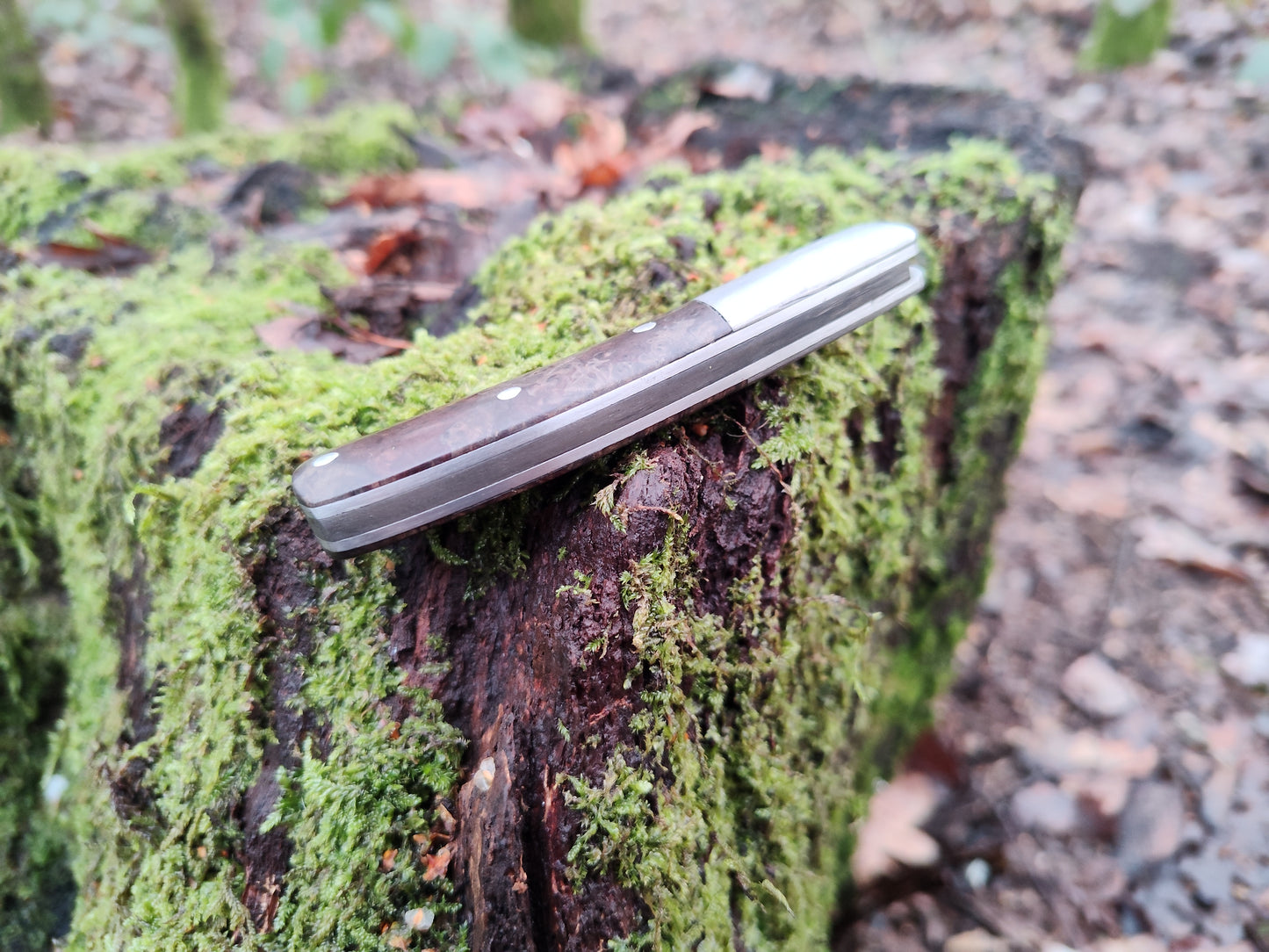 Hand-forged slipjoint folding knife with a pattern-welded blade. Wrought Iron Bolsters with Black Ash Burl Scales. Non-locking UK Legal Carry