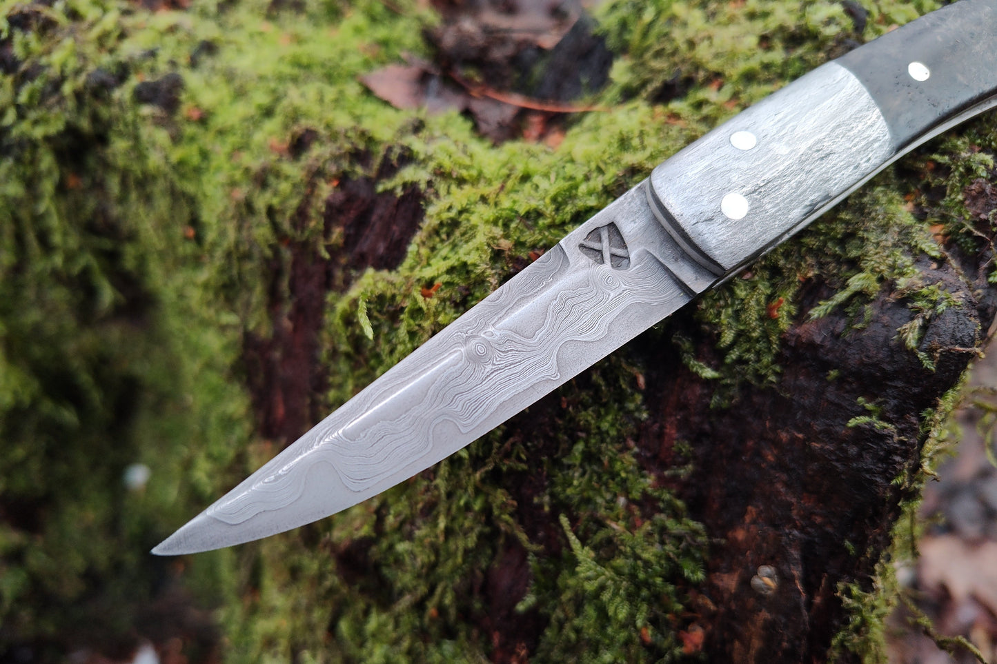Hand-forged slipjoint folding knife with a pattern-welded blade. Wrought Iron Bolsters with Black Ash Burl Scales. Non-locking UK Legal Carry