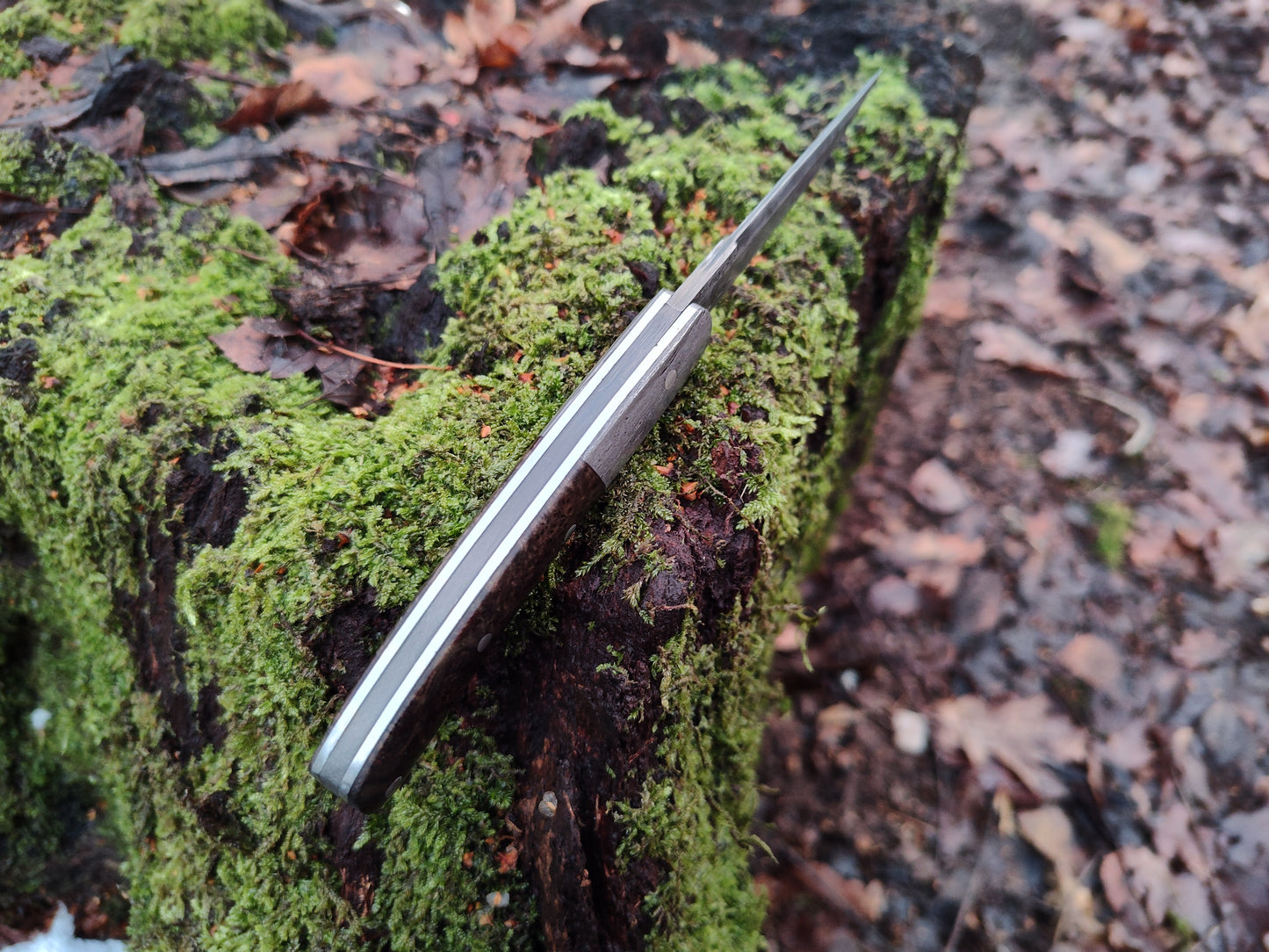 Hand-forged slipjoint folding knife with a pattern-welded blade. Wrought Iron Bolsters with Black Ash Burl Scales. Non-locking UK Legal Carry