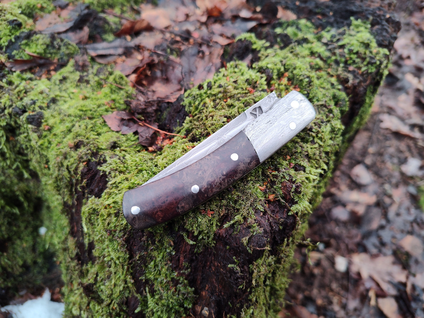 Hand-forged slipjoint folding knife with a pattern-welded blade. Wrought Iron Bolsters with Black Ash Burl Scales. Non-locking UK Legal Carry